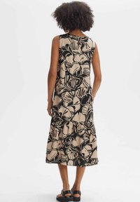 Sleeveless, tiered dress in beige with black floral pattern; lightweight fabric, round neckline, and button detail at back.