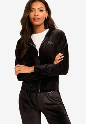 Black velour zip-up jacket with ribbed cuffs and hem, featuring a small logo on the left chest. Paired with matching velour pants.