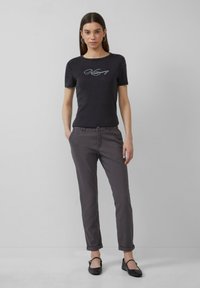 Donkergrijs katoenen T-shirt met een ronde halslijn en een versierde tekstgrafiek, gecombineerd met grijze broeken met opgerolde mouwen en zwarte flats.