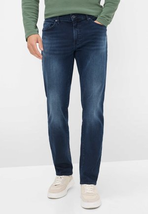 Donkerblauwe denim jeans met een rechte pasvorm, met voorzakken en subtiele vervaging. Gecombineerd met lichtgekleurde sneakers.