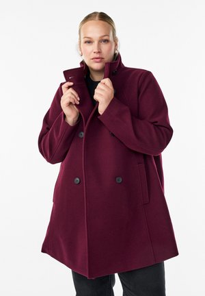 Burgundy double-breasted coat with a high collar, featuring black buttons and side pockets. Made from a textured, warm fabric.