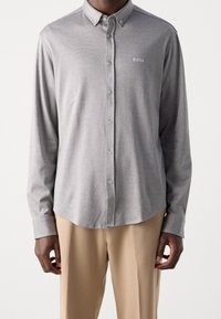 Grijze button-up shirt met een subtiel textuurpatroon, een standaard kraag en een klein "BOSS" logo op de borst, gecombineerd met beige broeken.