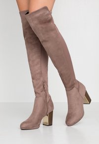 Botas hasta la rodilla de ante topo con tacón ancho brillante. Detalle de cremallera lateral y una combinación de tela suave y material liso.