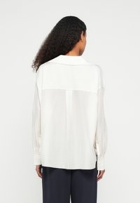 Hvit langermet skjorte med avslappet passform, med kontrasterende bakpanel og knapper på mansjettene, laget av lett stoff.