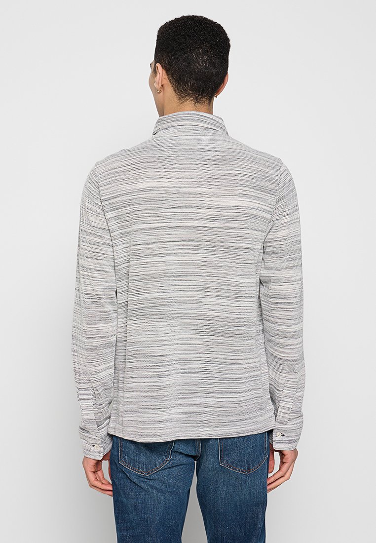 Graues Langarmshirt mit einem strukturierten, gestreiften Muster. Verfügt über einen Stehkragen und Knopfmanschetten. Kombiniert mit dunkler Jeans.