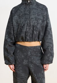 Veste noire courte avec motifs floraux, dotée d'un col montant et d'une fermeture éclair. Tissu texturé ajoutant un intérêt visuel. Pantalon assorti.