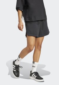 Čierne športové kraťasy a prehnane veľký top, doplnené čiernymi teniskami s bielymi pruhmi a bielymi ponožkami s čiernymi akcentmi.