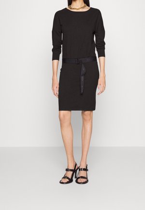 Robe noire à manches longues et silhouette ajustée, dotée d'une ceinture avec un logo. Associée à des sandales à talons hauts noires à brides.