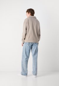 Hanorac de culoare bej deschis, cu guler, textură ribbed și croială lejeră, purtat împreună cu blugi largi de culoare albastră deschisă și teniși albi.