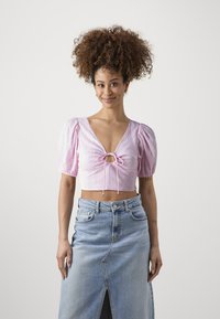 Lys rosa kort bluse med pufferm og en nøkkelhullfront, kombinert med et høy midje denimskjørt med en frontslitt.