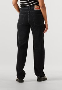 Jeans in denim nero con vestibilità dritta, cuciture visibili e due tasche posteriori. Presentano una patch in pelle con marchio sulla vita.
