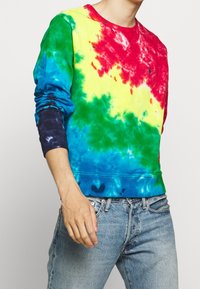 Flerfärgad tie-dye sweatshirt med mönster i röd, gul, grön och blå. Tillverkad av bomull med ribbade ärmslut och fåll. Avslappnad passform.