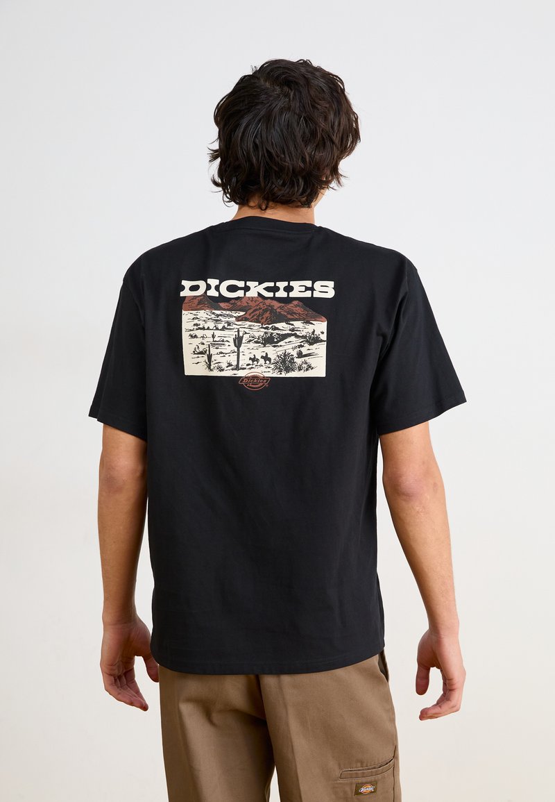 Juodas medvilnės marškinėliai su dideliu spalvotu piešiniu ant nugaros, vaizduojančiu dykumos peizažus ir prekės ženklo pavadinimą "DICKIES" balta spalva.