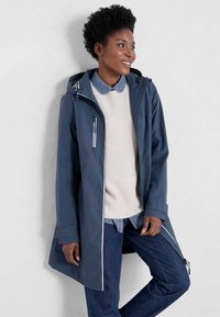 Granatowy wodoodporny płaszcz z zamkiem błyskawicznym z przodu i kapturem, z kontrastowymi szwami, zamykanymi kieszeniami i luźnym krojem na beżowy sweter.