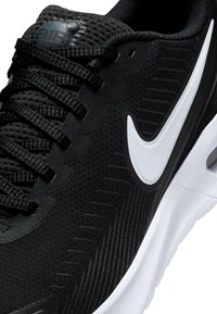 Chaussure de sport noire avec un dessus en maille texturée, logo Swoosh blanc et semelle rembourrée avec des rainures horizontales.