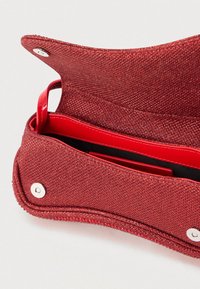 Geantă mică roșie, strălucitoare, cu clapeta deschisă, arătând captuseala interioară din piele roșie și închiderile magnetice, pe un fundal deschis.