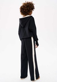 Zwarte hoodie met een losse pasvorm. Gecombineerd met zwarte wijde broek met witte zijkanten. Zachte stof, casual ontwerp.