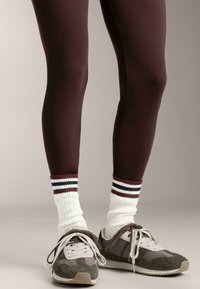 Leggings color borgogna, calzini bianchi a coste con strisce rosse e blu navy, e scarpe sportive grigie con dettagli bianchi e tomaie testurizzate.