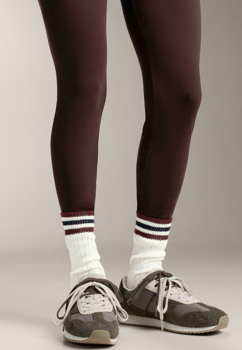 Leggings color borgogna, calzini bianchi a coste con strisce rosse e blu navy, e scarpe sportive grigie con dettagli bianchi e tomaie testurizzate.