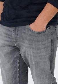 Vaqueros de mezclilla grises con diseño de pierna recta y cinco bolsillos, con una textura suave y un desvanecimiento sutil para un aspecto desgastado.