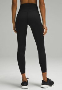 Black high-waisted leggings made of smooth, stretchy material with a fitted design. Worn with black athletic shoes.
