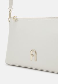 Bílá kabelka clutch z umělé kůže se zlatým kovovým hardwarovým doplňkem, která se vyznačuje minimalistickým designem a výrazným embosovaným logem.