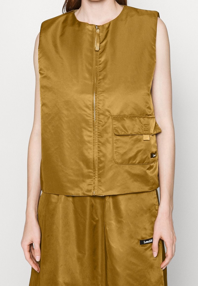 Sleeveless golden-brown zip-up vest made of shiny fabric, featuring a front pocket and subtle branding detail. Textured finish, minimal design.