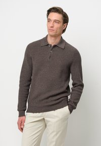 Pulóver marrón de punto acanalado con cuello y tapeta de tres botones, combinado con pantalones de color claro. Presenta mangas largas y un acabado texturizado.