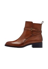Bottine en cuir marron avec une silhouette épurée, des accessoires en or et un petit talon bloc. Dispose d'une languette pour un enfilage facile.