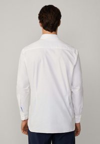 Camicia bianca a maniche lunghe con orlo curvo, polsini abbottonati e accento blu all'interno del colletto. Tessuto liscio, design formale, retro semplice.