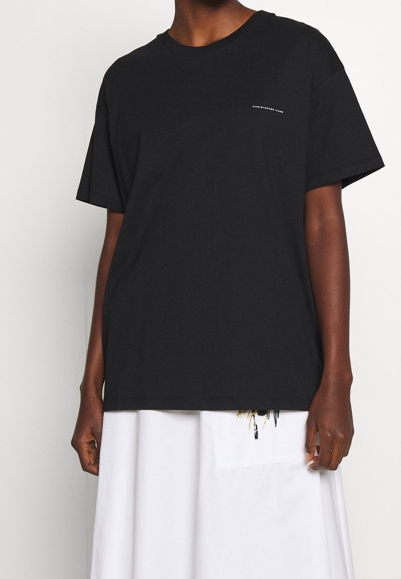 Personne portant un t-shirt noir ample avec un petit texte blanc sur la poitrine gauche et une jupe blanche avec une grande poche avant.