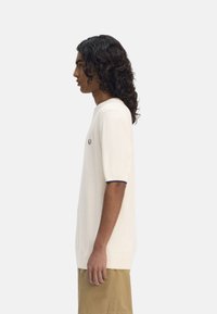Maglietta a maniche corte di colore crema in maglia, con colletto a coste e dettagli navy, abbinata a pantaloni corti beige.