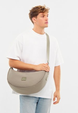 Borsa a tracolla grigia realizzata in tessuto resistente, con design curvato, tracolla regolabile e una piccola etichetta metallica sul davanti.