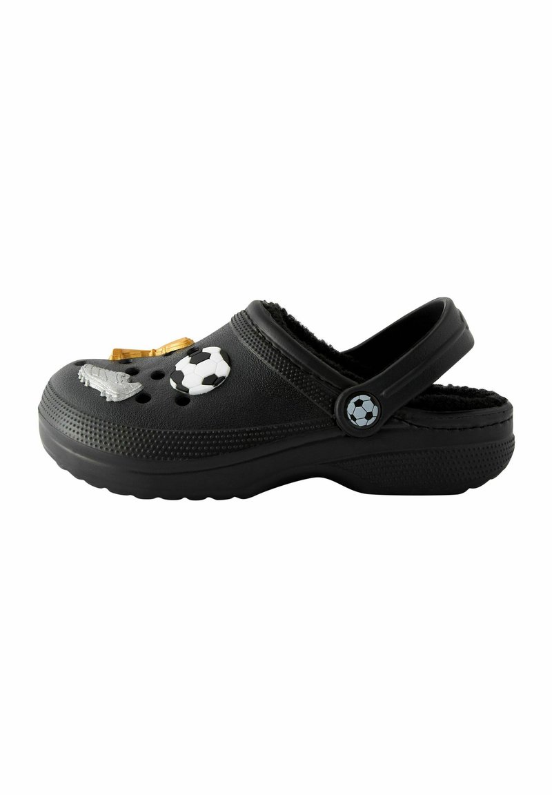 Zueco negro hecho de goma, con múltiples agujeros para ventilación. Decorado con charms de temática futbolística, incluyendo un balón y el logo del equipo.