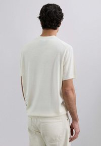 Suéter de punto de manga corta color beige claro con una textura suave. Cuello redondo y corte holgado, combinado con pantalones de color claro. Diseño liso, sin patrones.