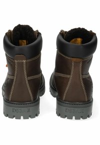 Botas de cuero marrón hasta el tobillo con una suela de goma negra texturizada, costuras en contraste y un forro de piel sintética en la parte superior.