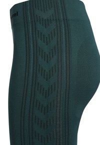 Donkergroene leggings van textuurstof met een patroon van verticale lijnen en chevronontwerpen langs de zijkanten.