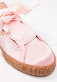 Gros plan d'une basket en satin rose avec de larges lacets ruban en satin et une semelle en caoutchouc texturée marron.