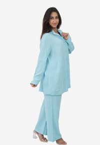 Jasnoniebieski, teksturowany dwuczęściowy zestaw składający się z koszuli z długim rękawem zapinanej na guziki oraz pasujących szerokich spodni. Przezroczyste klapki na obcasie.