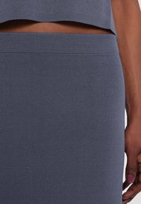 Gray knit skirt with a textured surface, featuring a fitted design and a smooth waistband, partially covered by a matching top.