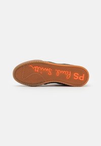 Schwarze Sneakersohle mit Fischgrätmuster, ausgestattet mit einem orangefarbenen "PS"-Logo und Text. Die Sohle besteht aus Gummi mit einer strukturierten Oberfläche.