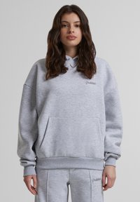 Šviesiai pilkas hoodie pagamintas iš minkštos medžiagos, su priekinėmis kišenėmis, raukšlėtomis rankovėmis ir su atitraukiamu gobtuvu. Išsiuvinėtas tekstas ant krūtinės.