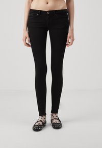 Jeans skinny negros con cinco bolsillos, cierre de cremallera y un brillo sutil. Combinados con bailarinas negras y calcetas transparentes con estampado.