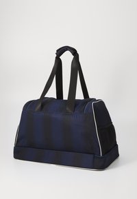 Marine-randete duffelbag med sorte stoffstropper, polstrede håndtak, mesh sidelomme og hvit trim langs bunnkanten og glidelåsen.
