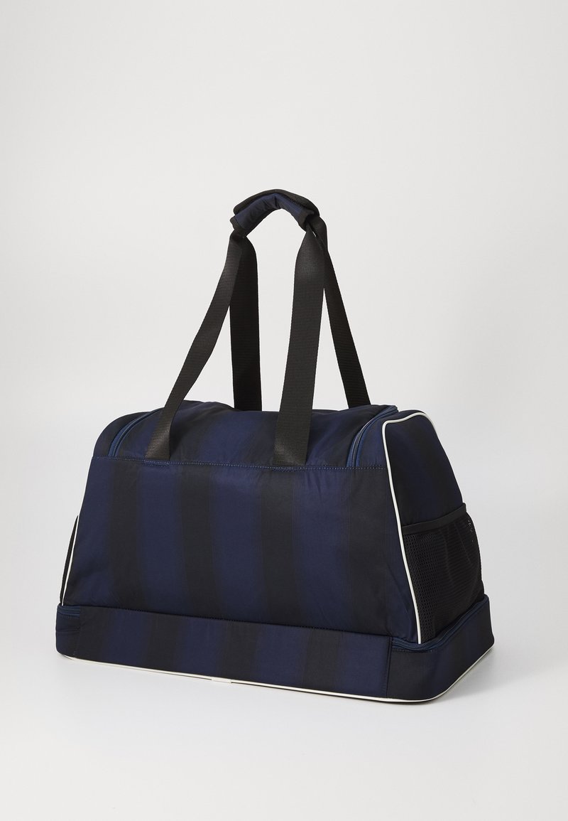 Sac de voyage rayé marine avec des sangles en tissu noir, des poignées rembourrées, une poche latérale en maille et un bord blanc le long du bas et de la fermeture éclair.