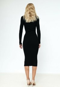 Robe en tricot côtelé noire à manches longues, silhouette ajustée, ourlet mi-genoux, associée à des escarpins nude.
