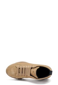 Zapatilla de ante marrón con punta redonda, suela de goma y cordones elásticos. Presenta una pequeña lengüeta negra en el talón y un upper texturizado para mayor agarre.