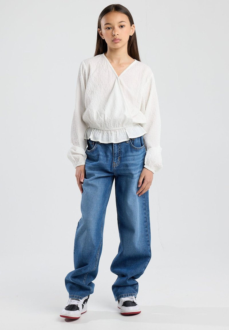 Top lungo bianco e texturizzato con orlo arricciato abbinato a jeans chiari a vestibilità comoda e sneakers bianco e nere.