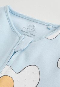 Ljusblå bebisklädsel med tryckknappsstängning, med ett mönster av tecknade ägg i vitt och gult. Mjuk bomullsmaterial.