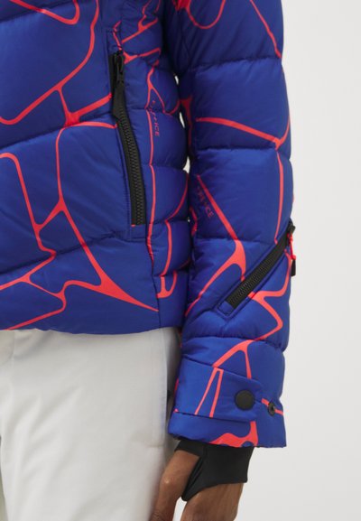 Blauer Puffjacke mit roten abstrakten Linien, ausgestattet mit zwei Reißverschlusstaschen und einem schwarzen Knopfmanschettendetail.